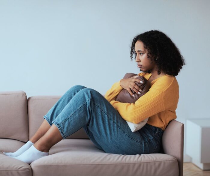 A young woman curled up on a sofa, hugging a pillow